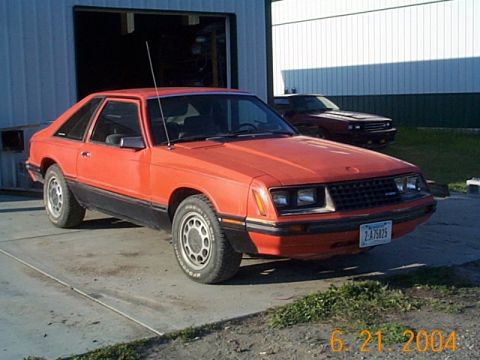 1983 Mercury Capri - An orange coupe is parked in front of a garage, with a second red coupe visible in the background.