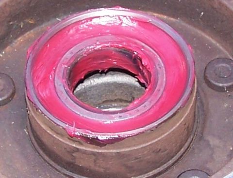 1990 Ford Bronco - Close-up view of a wheel bearing assembly being packed with pink grease.