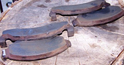 1990 Ford Bronco - Used brake pads are shown on a wooden surface, indicating wear and tear.