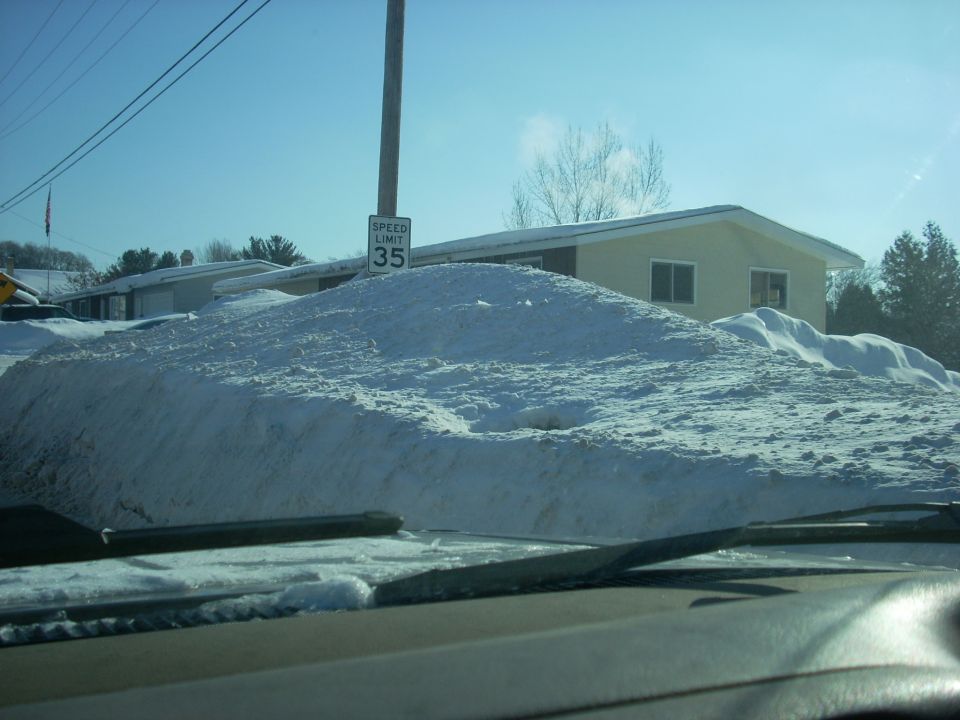 Snow pile obscures vehicle; speed limit 35 sign visible
