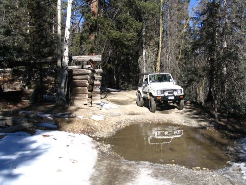 1987 Suzuki Samurai - A white Suzuki Samurai is parked on a dirt road in a wooded area, with a reflection visible in a puddle.