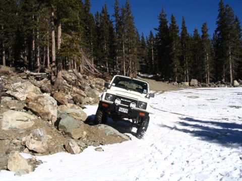 1987 Suzuki Samurai - A white 1987 Suzuki Samurai tackles a challenging off-road course with snow and rocks.