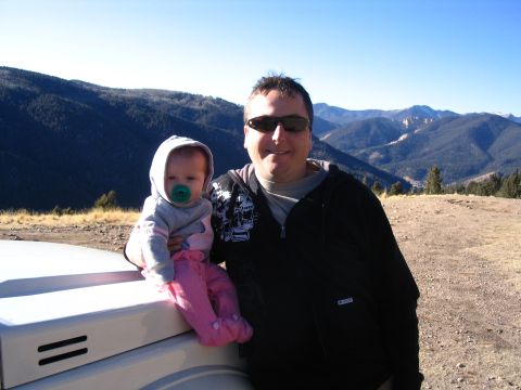 1987 Suzuki Samurai - Man and baby posing on the hood of a vehicle with a mountain landscape behind them.