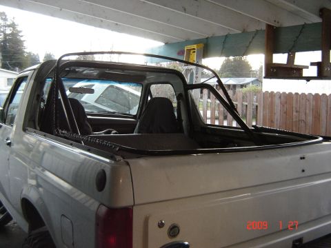 1993 Ford Bronco - The rear section of a white Ford Bronco is visible, a black roll cage and a soft top frame.