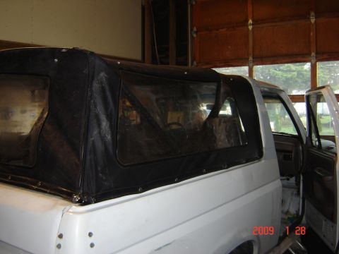 1993 Ford Bronco - White Ford Bronco with a black soft top is parked inside a garage, showing its side profile and open driver's door.