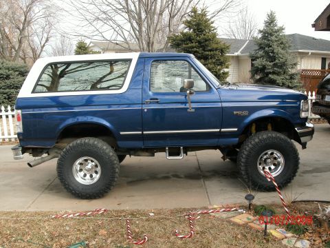 1996 Ford Bronco - A lifted blue Ford Bronco with a white hardtop is parked on a driveway.