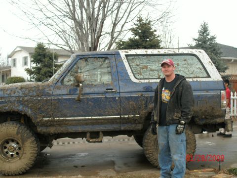 1996 Ford Bronco - A man stands next to a heavily mud-covered blue Ford Bronco with a white top.