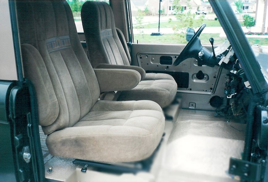 Pair of tan cloth bucket seats and bare metal door panel inside a stripped SUV interior