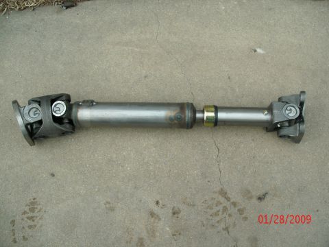 1996 Ford Bronco - A driveshaft with universal joints and a yellow band is shown on a concrete surface.