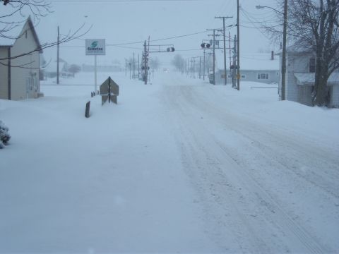 1996 Ford Bronco - A street is covered in snow with houses and utility poles lining the sides.