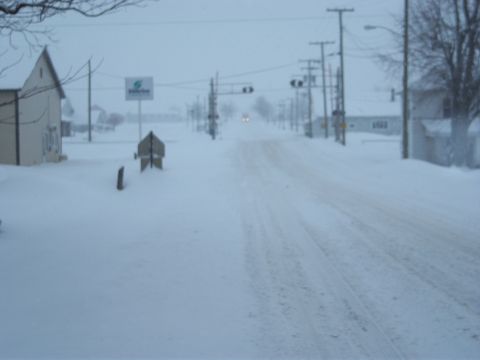 1996 Ford Bronco - A snow-covered road stretches into the distance under a cloudy sky, with a few distant headlights visible headlights.