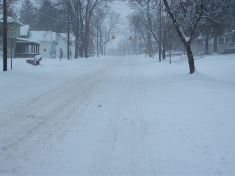 1996 Ford Bronco - A street is covered in snow, with houses and trees lining the sides.