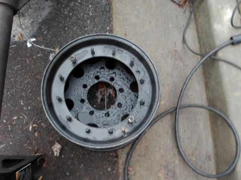 1990 Ford Bronco - A close-up view of a spare tire rim, showing its lug nut holes and a wet surface.