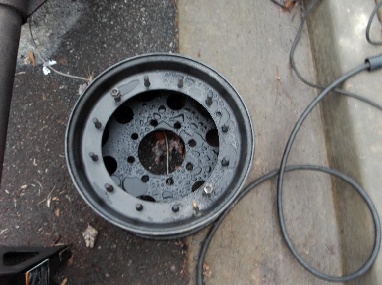 black spare tire rim with water droplets on it sits on the ground next to some cables