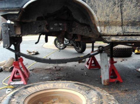 1990 Ford Bronco - A vehicle's undercarriage is supported by jack stands, revealing its leaf spring suspension system.