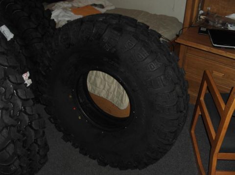 1990 Ford Bronco - Several large off-road tires are stacked indoors, with a dresser and chair visible in the background.
