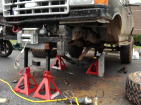 1990 Ford Bronco - Front view of a black Ford truck undergoing maintenance, supported by red jack stands.