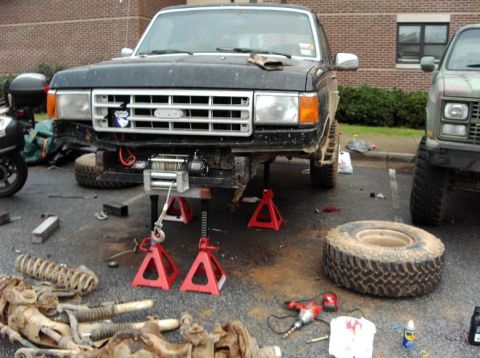 1990 Ford Bronco - Front end of a 1990 Ford Bronco is raised on jack stands for repairs, with parts scattered around.