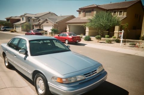 1997 Ford Crown Victoria - A silver sedan is parked on a residential street with houses in the background.