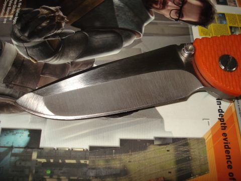 2000 Ford Crown Victoria - A close-up view of a knife blade and its textured orange handle, resting on a surface with printed text and images.