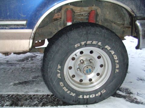 1996 Ford Bronco - Close-up of the wheel and suspension system of a blue vehicle on a snowy surface.
