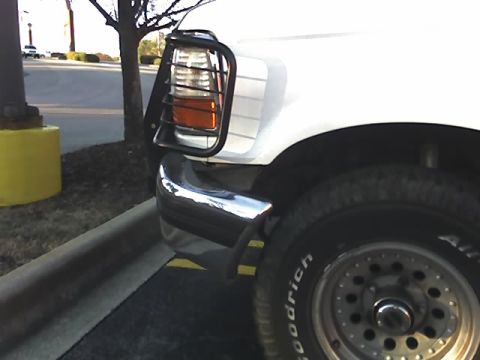 1996 Ford Bronco - The front corner of a white SUV is visible, parked near a curb and a yellow bollard.