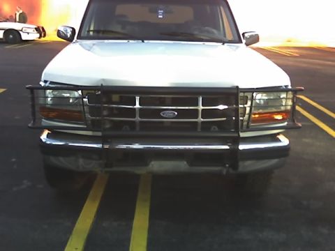 1996 Ford Bronco - Front view of a 1996 Ford Bronco equipped with a brush guard, with a police car visible in the background.