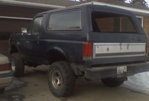 1988 Ford Bronco - This dark blue Ford Bronco from 1987 features a lifted suspension and aggressive off-road tires, viewed from the rear.
