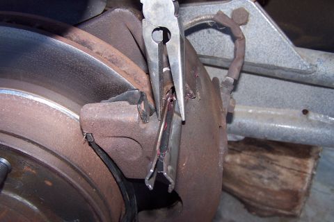 1990 Ford Bronco - Close-up of a vehicle's brake system, showing a caliper and rotor with pliers in use.
