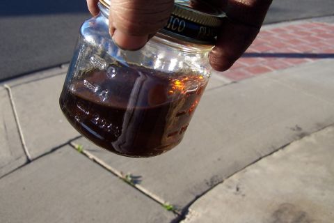 1990 Ford Bronco - A hand holds a glass jar filled with a dark, amber-colored liquid, possibly oil or fluid.