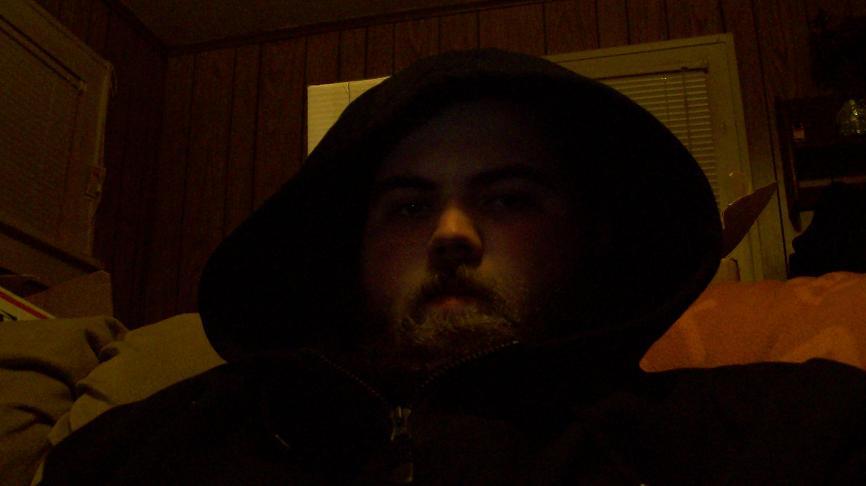 Bearded man in a dark hood in a dim wood-paneled room