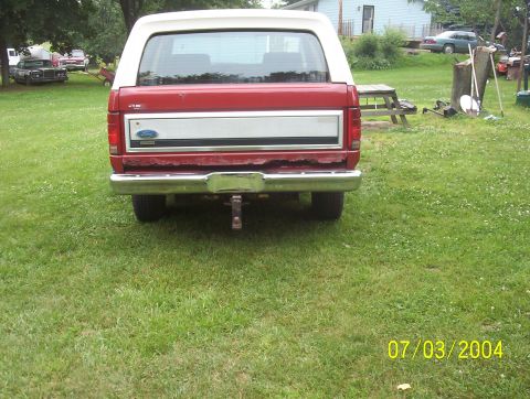 1985 Ford Bronco - Rear view of a 1985 Ford Bronco parked on grass, with other vehicles and a picnic table in the yard.