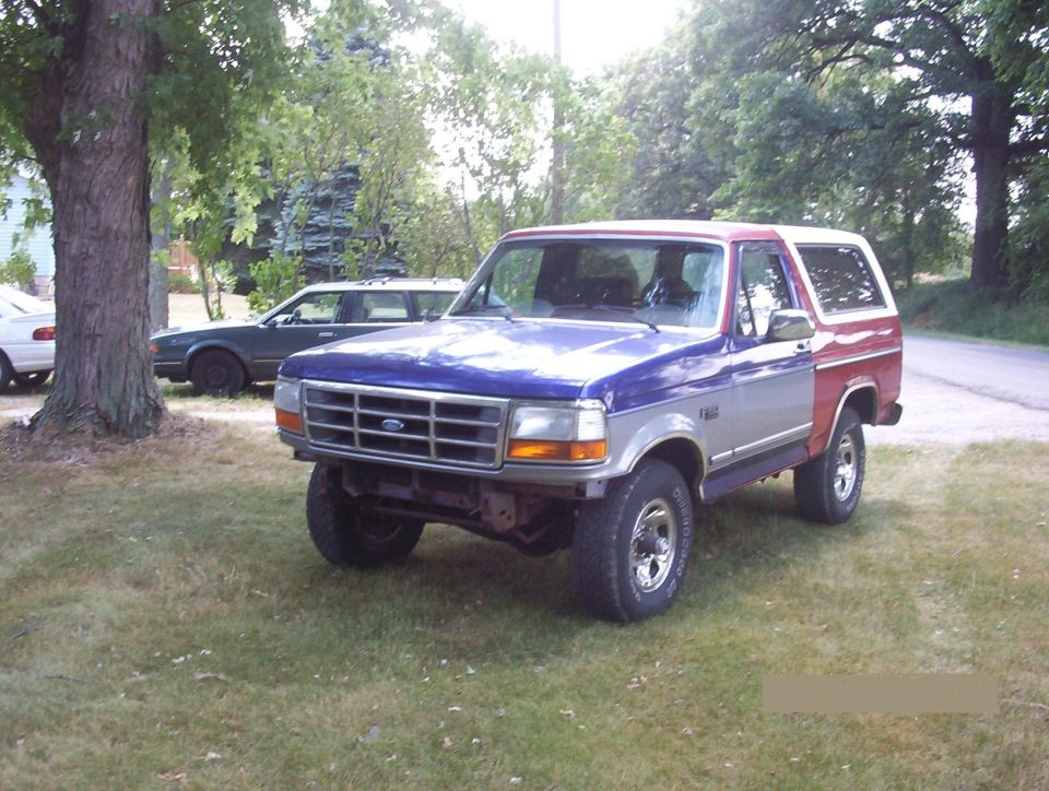 Ford Bronco with blue hood, silver sides, and red rear quarter panels parked on grass