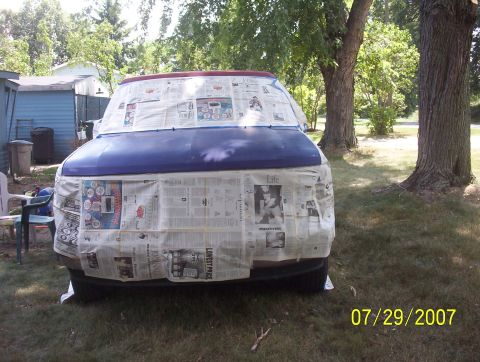 1985 Ford Bronco - A van is covered in newspaper, likely for painting, in a grassy yard with trees.