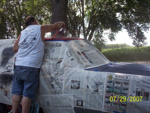 1985 Ford Bronco - A person is spray painting a vehicle that is covered in newspaper for protection.