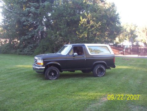 1985 Ford Bronco - A black Ford Bronco with a white top is parked on a grassy lawn.