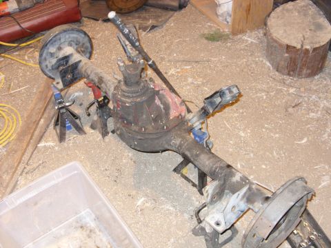1988 Ford Bronco - A disassembled vehicle rear axle assembly is shown supported by jack stands on a floor covered in wood shavings.