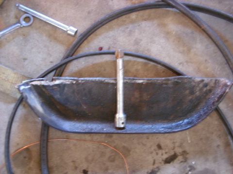 1988 Ford Bronco - A metal part, possibly from a vehicle, lies on the ground with a socket wrench and a hose.