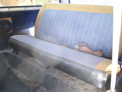 1979 Ford Bronco - The interior of a vehicle shows a rear bench seat with a distinctive striped pattern and worn vinyl trim.