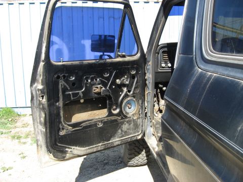 1979 Ford Bronco - The driver's side door is open, revealing the interior of a black vehicle with its door panel removed and a glimpse of the dashboard.