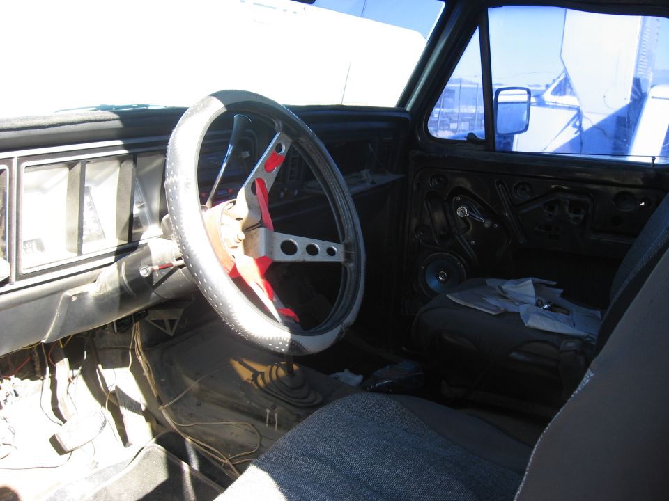 1979 Ford Bronco interior showing aftermarket steering wheel, worn seat, and door panel removed
