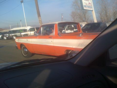 1983 Ford Bronco - An orange and white pickup truck is seen from inside another vehicle at what appears to be a car dealership.