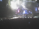 2004 Land Rover Land Rover - A wide shot captures a band performing on a brightly lit stage in front of a packed arena.