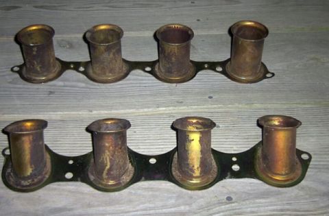 1997 Ford Taurus - Two brass-colored, four-cylinder intake manifolds are shown mounted on a dark metal plate, resting on a wooden surface.