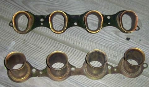 1997 Ford Taurus - Two intake manifold gaskets are shown on a wooden surface. The top gasket is black with four oval openings, and the bottom gasket is brass…