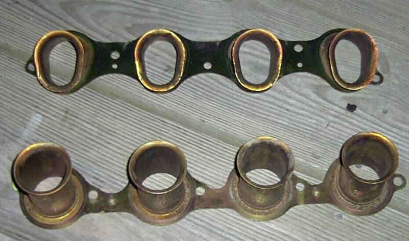 Two brass and black intake manifold gaskets on a wooden surface
