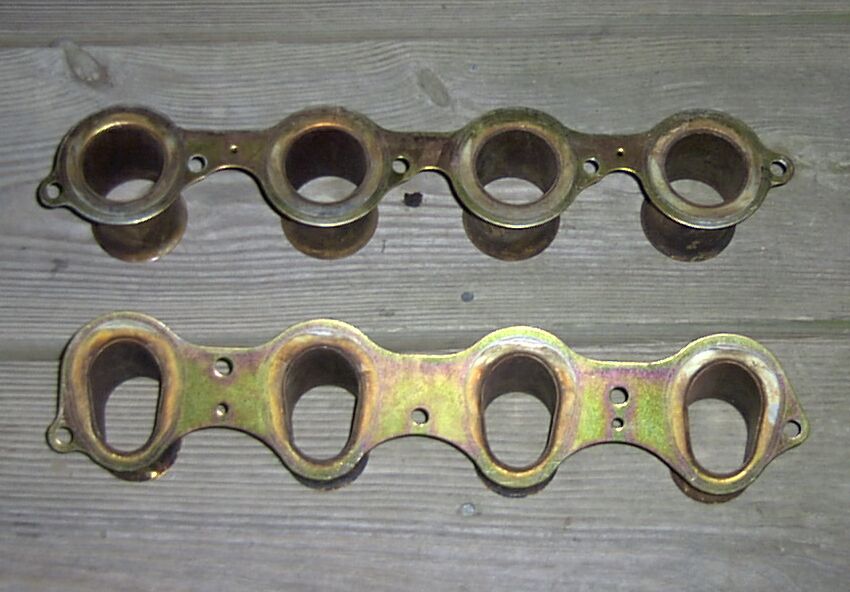 Two intake manifold gaskets on a wooden surface. Top has four round openings, bottom has four oval openings.