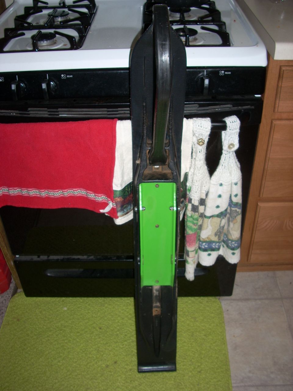 Black and green snowmobile ski in front of a stove with towels.