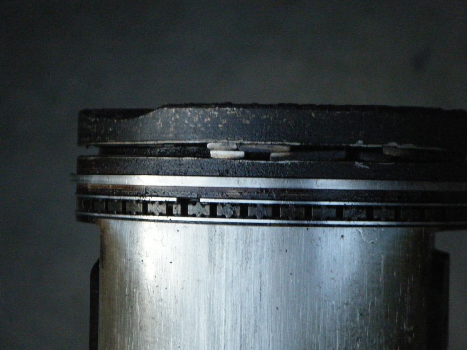 Close-up of piston top edge showing ring grooves, oil ring expander segments, and carbon buildup