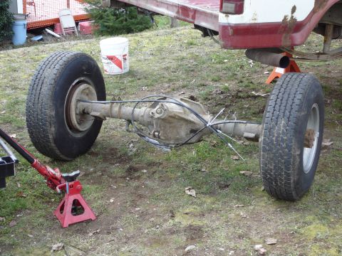 1991 Ford Bronco - The rear axle assembly of a vehicle, complete with tires and brake lines, is supported by jack stands on the ground. The vehicle's frame an…